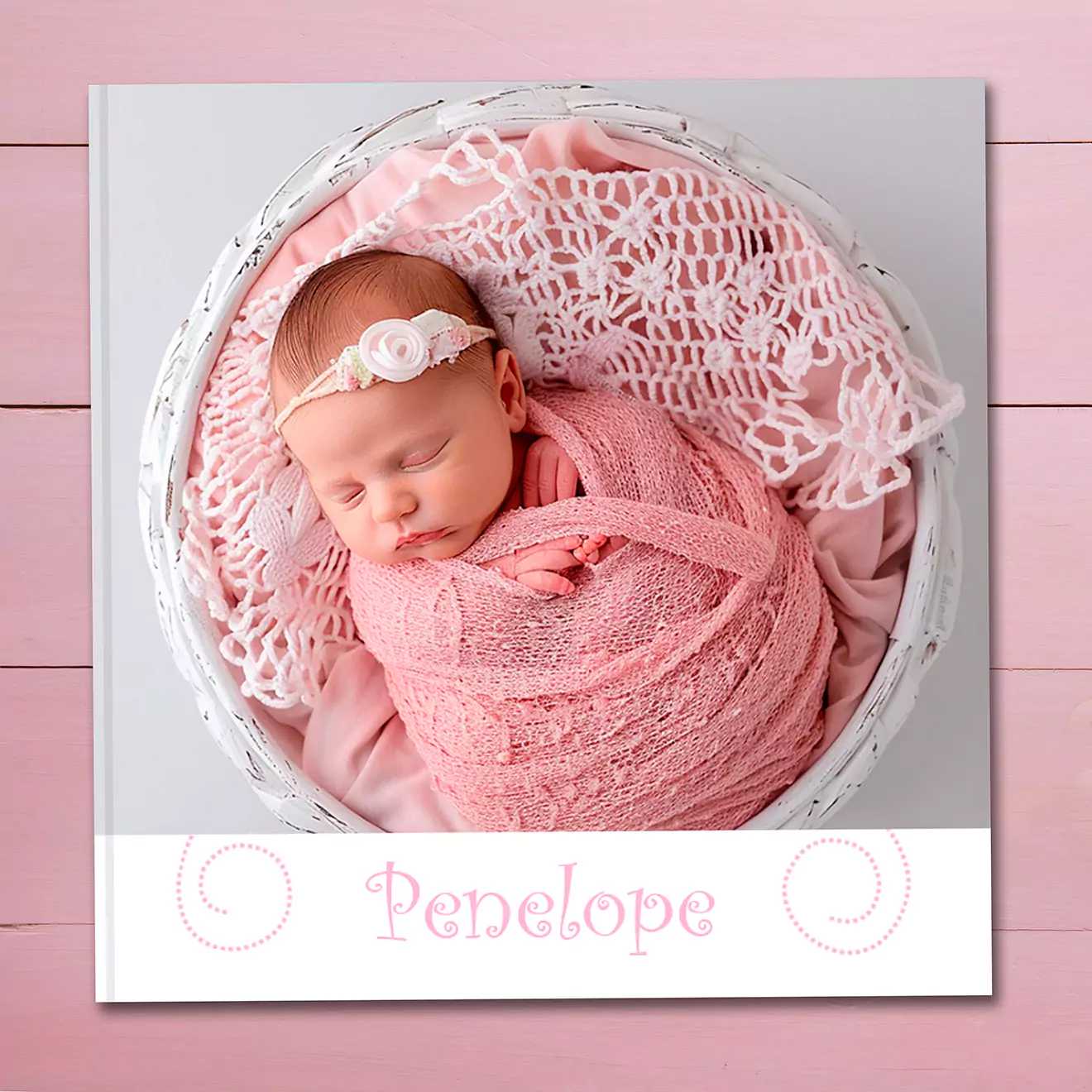 Square photobook with a pink cover featuring a baby girl in a light pink dress and headband. The title on the cover reads 'Pretty Little Penelope - My First Birthday' in a playful font.