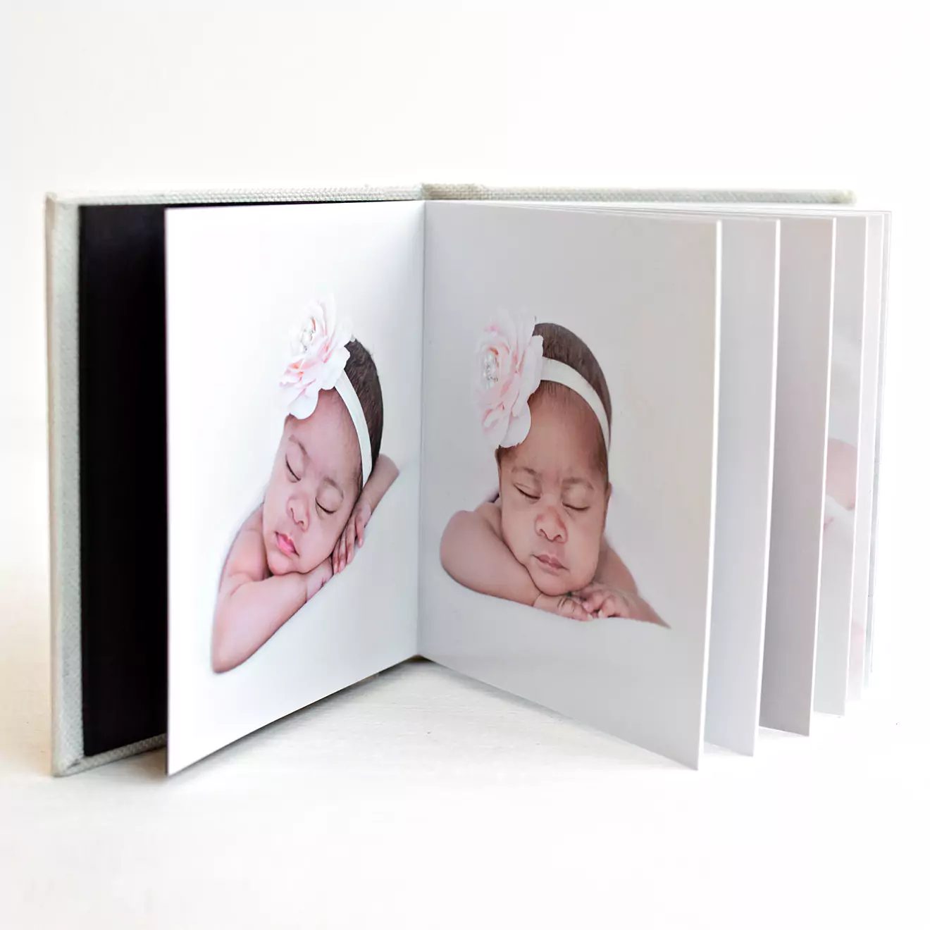 Open baby photo album with a soft cover, displaying a high-quality image of a sleeping infant. The album is placed on a light pink surface, accompanied by baby accessories including a brush, eucalyptus branch, and a white bunny teether. Ideal for baby shower gift ideas and personalised gifts in South Africa.