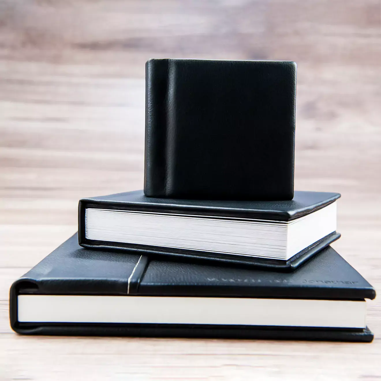 A set of three black leather-bound photo albums of varying sizes stacked on a wooden surface. The albums feature a sleek, minimalist design with white pages, making them ideal for preserving memories. Perfect for gifts for men, baby shower gift ideas, or personalised gifts in South Africa.