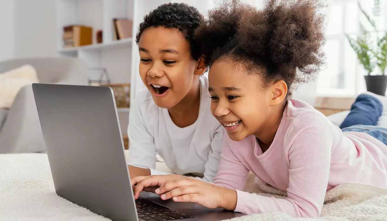 Two young children smiling while creating a photo book on a PC - banner