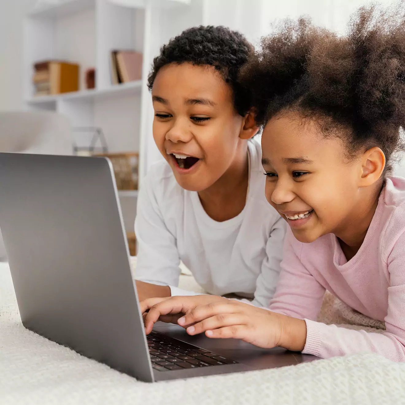 Two young children smiling while creating a photo book on a PC