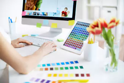 Person using a Mac with a colour chart beside her, calibrating her monitor for accurate colour representation