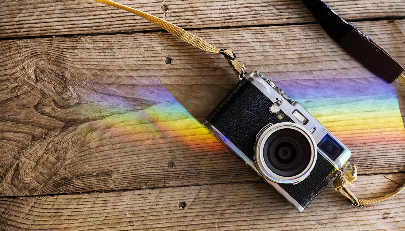 Vintage-style camera on a wooden deck with a beautiful rainbow in the background - banner